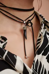 Gargantilla negra de múltiples tiras finas con dije de colmillo negro con base plateada.