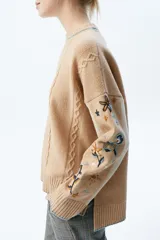 Sweater beige de tejido de punto con mangas bordadas a mano con flores de colores.