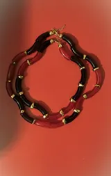 Collar de dos vueltas con eslabones tubulares curvos, alternando colores negro y rojo translúcido, separados por pequeños detalles metálicos dorados.