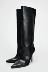 Bota negra de caña alta, confeccionada en cuero sintético, con terminación en punta y tacón fino.