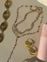 Set de dos collares dorados: uno tipo choker con esferas y otro tipo corbatín con dije de cadena con piedras de colores.