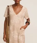 Vestido corto tipo t-shirt color beige con estampado de follaje y arquitectura, escote en V y mangas cortas.