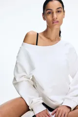 Buzo blanco con escote off-the-shoulder, hombros caídos, corte holgado y mangas largas con puños ajustados.