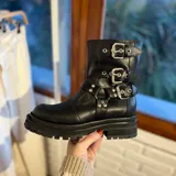 Botas cortas negras de cuero con suela track, caña media y tres correas con hebillas plateadas.