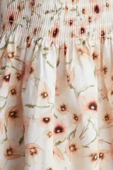 Vestido midi blanco con estampado floral en tonos naranja y marrón. Tiene breteles finos, escote recto y cuerpo fruncido con elástico en el busto.