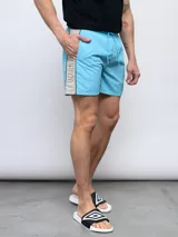 Short de baño celeste con corte lateral en gris y logo de Umbro estampado en vertical.
