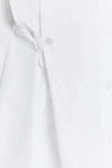 Camisa blanca de cuello solapa y manga larga. Detalle de pliegues con botones. Cierre frontal con botones.
