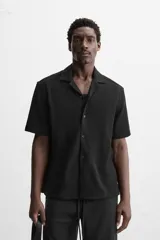 Camisa color crudo de corte regular fit, confeccionada en tejido con textura. Tiene cuello bowling, manga corta, bajo con aberturas laterales y cierre frontal con botones.