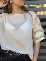 Blusa color crema de mangas cortas con detalle de rosas en relieve en las mangas.