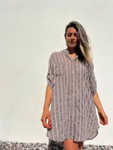 Camisero corto color habano con bordado de líneas verticales blancas. Tiene cuello camisero, mangas cortas y cierre frontal con botones.