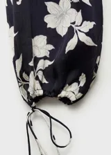 Blusa de satén color negro con estampado de flores blancas, cuello redondo, cierre frontal con botones, manga larga con puños elásticos y fruncidos, y corte recto.