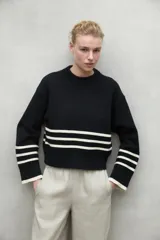 Sweater color crema con rayas horizontales negras en el pecho y los puños, de corte holgado y cuello redondo.