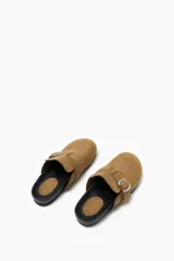 Zueco color beige con hebilla metálica ajustable, confeccionado en material símil gamuza y suela de goma negra.
