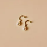 Par de aros colgantes de oro amarillo 18k con perlas de cultivo blancas. El aro es de tipo medio aro y la perla cuelga del mismo.