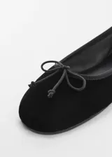 Zapato flat de terciopelo negro con lazo decorativo en la parte frontal y punta redonda.