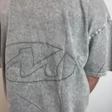 Remera gris con efecto gastado, corte boxy y estampado ovalado en la espalda.