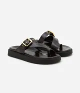 Sandalias planas de PU color marrón oscuro, con tira entre los dedos y tira ancha sobre el empeine con hebilla dorada ajustable.
