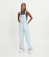 Mono largo de jeans celeste claro, con tirantes ajustables, bolsillo frontal con solapa y bolsillos laterales.