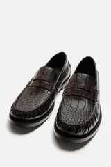 Mocasín de vestir color marrón oscuro con estampado de cocodrilo, horma redonda y suela con ligero tacón.