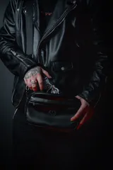 Bandolera negra de cuero sintético con correa ancha ajustable y desmontable. Cuenta con cierre superior, bolsillo frontal con tiracierre customizado, forro interno y cuatro bolsillos en total (dos exteriores y dos interiores).