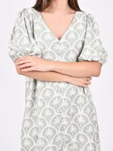 Vestido corto color verde con estampado de palmeras blancas, escote en V y mangas cortas abullonadas.