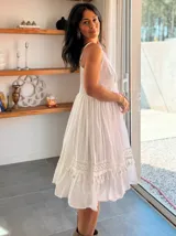 Vestido corto blanco de algodón, con tirantes finos, corpiño ajustado con frunces y falda con vuelo y detalles de encaje y borlas en el ruedo.