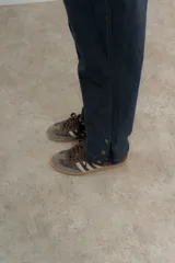Pantalón de jean azul oscuro de corte recto con detalle de botones dorados en el tobillo.