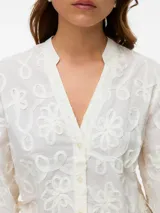 Camisa blanca de manga larga con cuello en V, cierre frontal con botones, puños abotonados y bordado floral.