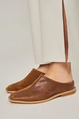 Zuecos color beige confeccionados en cuero vacuno, con punta cuadrada y suela plana color negro.