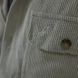 Camisa celeste de pana con corte oversize, cuello clásico, cierre frontal con botones, dos bolsillos con solapa en el pecho y mangas largas con puños abotonados.