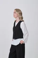 Chaleco negro de poliéster con escote en V y cierre frontal de botones. Diseño holgado.