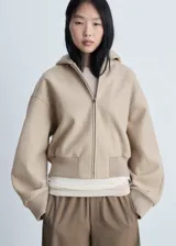 Chaqueta con capucha color beige, con cierre frontal de cremallera, cuello alto, puños elásticos y diseño oversize.