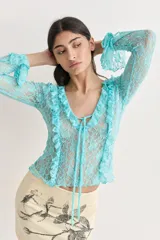 Top de manga larga color celeste/turquesa, confeccionado en tejido de encaje floral. Presenta escote en V con volados en el borde y lazos ajustables en el centro del escote y en los puños.