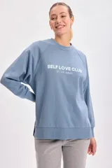 Buzo deportivo celeste con cuello redondo y mangas largas. Estampa frontal con la frase "Self Love Club, do not disturb" en letras blancas. Corte oversize con aberturas laterales.