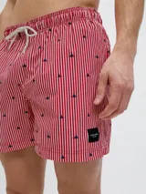 Short de baño rojo y blanco a rayas verticales con pequeños dibujos de veleros negros. Tiene cintura elástica con cordón ajustable.