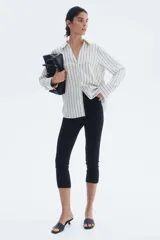Blusa de manga larga a rayas verticales blancas y negras, con cuello clásico, escote en V y cierre frontal con botones. Puños con detalle de rayas horizontales y bajo redondeado.