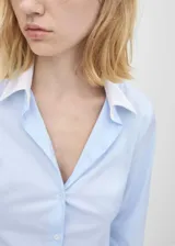 Camisa celeste de popelina de algodón con cuello y puños blancos en contraste, manga larga con puños abotonados, corte recto, cierre frontal con botones y diseño entallado.