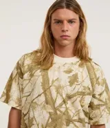 Remera de algodón color crudo con estampado de ramas y hojas en tonos marrones. Corte boxy, cuello redondo y mangas cortas.