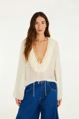 Blusa color crema con escote en V pronunciado y volantes en los bordes. Mangas largas amplias.