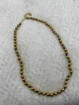 Collar corto de perlas doradas con hilo de seda azul marino y cierre de mosquetón dorado con cadena de extensión.