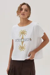Remera blanca de algodón con estampa de palmeras y la palabra "Sunrise" en el frente.