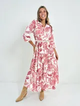 Vestido largo camisero con estampado floral en tonos rosados y blancos, con cuello camisero, manga 3/4 y falda escalonada. Incluye cinturón fino de soga.