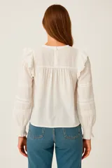 Blusa blanca de algodón con escote redondo, mangas largas abullonadas con puños elásticos y detalles de encaje calado en el frente y las mangas.