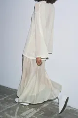 Vestido largo de punto ligero color crudo, con cuello redondo y mangas largas. Presenta un forro interior de tela satinada color beige claro que asoma en el bajo, creando un efecto de dos piezas.