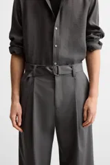 Pantalón negro de corte ancho con cinturón de tela con hebilla metálica y pliegues frontales.