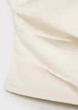 Top de algodón color crema, con cuello asimétrico, detalle de bordado floral en el hombro y frunces laterales. Cierre lateral con cremallera.