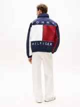 Campera náutica amplia reversible de nailon, con diseño color block en rojo, blanco y azul marino. Tiene capucha fija, cierre de cremallera oculto con botones a presión, puños y bajo elásticos, dos bolsillos ribeteados en la cintura, parche con logo de Tommy Hilfiger en el pecho y logo de Tommy Hilfiger en el cuello, las mangas y la espalda.