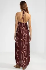 Vestido largo color borgoña con estampado de cadenas y flores rosadas. Tiene cuello halter con cordón ajustable y una insignia removible de Polonio.