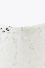Top de encaje blanco con cuello redondo, mangas largas abullonadas y puños con botones metálicos.