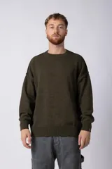 Sweater de punto color verde oliva, de corte holgado y mangas largas. Tiene cuello redondo y puños y ruedo acanalados.